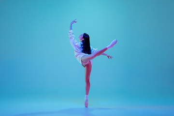 Image showing Young and graceful ballet dancer isolated on blue studio background in neon light. Art, motion, action, flexibility, inspiration concept.