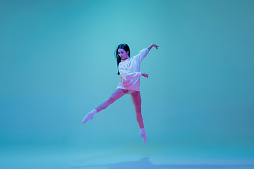 Image showing Young and graceful ballet dancer isolated on blue studio background in neon light. Art, motion, action, flexibility, inspiration concept.