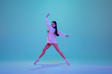 Image showing Young and graceful ballet dancer isolated on blue studio background in neon light. Art, motion, action, flexibility, inspiration concept.