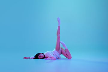 Image showing Young and graceful ballet dancer isolated on blue studio background in neon light. Art, motion, action, flexibility, inspiration concept.