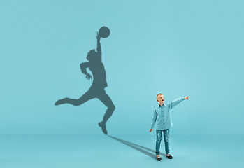 Image showing Childhood and dream about big and famous future. Conceptual image with boy and shadow of fit male basketball player on blue background