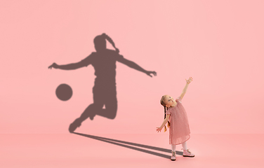 Image showing Childhood and dream about big and famous future. Conceptual image with girl and shadow of fit female football player on coral pink background