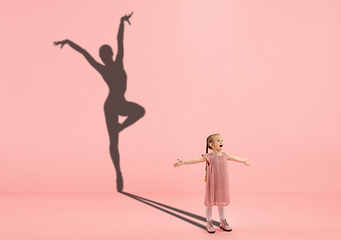 Image showing Childhood and dream about big and famous future. Conceptual image with girl and shadow of fit female ballet dancer on coral pink background