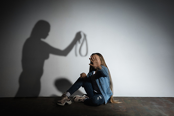 Image showing Domestic violence, abusing. Scared little caucasian girl, victim sitting close to white wall with shadow of angry mother\'s threatening on it.