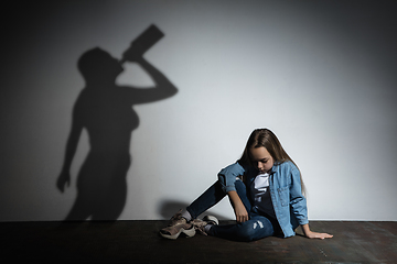 Image showing Domestic violence, abusing. Scared little caucasian girl, victim sitting close to white wall with shadow of angry threatening mother with alcohol addiction.