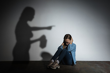 Image showing Domestic violence, abusing. Scared little caucasian girl, victim sitting close to white wall with shadow of angry threatening mother with alcohol addiction.