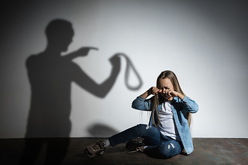 Image showing Domestic violence, abusing. Scared little caucasian girl, victim sitting close to white wall with shadow of angry father\'s threatening on it.