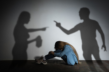 Image showing Domestic violence, abusing. Scared little caucasian girl, victim sitting close to white wall with shadow of angry threatening parents with alcohol addiction.