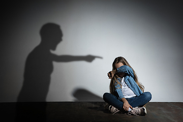 Image showing Domestic violence, abusing. Scared little caucasian girl, victim sitting close to white wall with shadow of angry father\'s threatening on it.