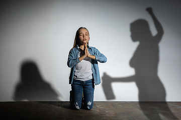 Image showing Domestic violence, abusing. Scared little caucasian girl, victim sitting close to white wall with shadow of angry threatening mother with alcohol addiction.