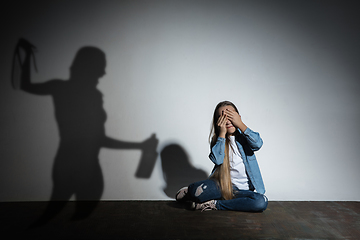 Image showing Domestic violence, abusing. Scared little caucasian girl, victim sitting close to white wall with shadow of angry threatening mother with alcohol addiction.