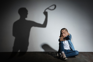 Image showing Domestic violence, abusing. Scared little caucasian girl, victim sitting close to white wall with shadow of angry father\'s threatening on it.