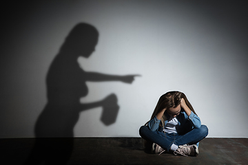 Image showing Domestic violence, abusing. Scared little caucasian girl, victim sitting close to white wall with shadow of angry threatening mother with alcohol addiction.