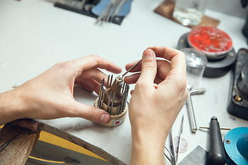 Image showing Close up hands of jeweller, goldsmiths making of golden ring with gemstone using professional tools.