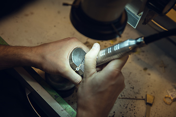 Image showing Close up hands of jeweller, goldsmiths making of golden ring with gemstone using professional tools.