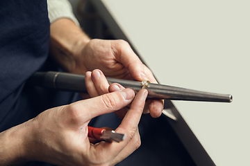 Image showing Close up hands of jeweller, goldsmiths making of golden ring with gemstone using professional tools.