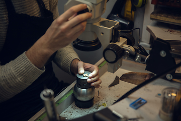 Image showing Close up hands of jeweller, goldsmiths making of golden cross with gemstone using professional tools.