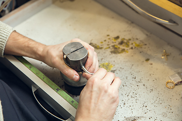 Image showing Close up hands of jeweller, goldsmiths making of golden ring with gemstone using professional tools.