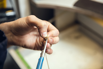 Image showing Close up hands of jeweller, goldsmiths making of golden ring with gemstone using professional tools.