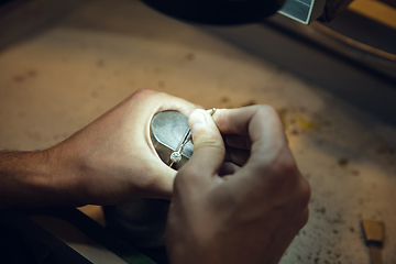 Image showing Close up hands of jeweller, goldsmiths making of golden ring with gemstone using professional tools.