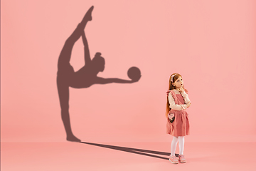 Image showing Childhood and dream about big and famous future. Conceptual image with girl and shadow of fit female rhythmic gymnast on coral pink background