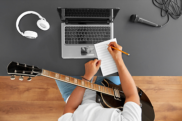 Image showing man with guitar writing to music book at table