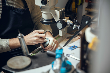 Image showing Close up hands of jeweller, goldsmiths making of golden ring with gemstone using professional tools.