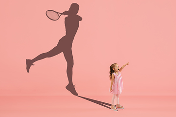 Image showing Childhood and dream about big and famous future. Conceptual image with girl and shadow of fit female tennis player on coral pink background