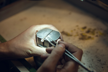 Image showing Close up hands of jeweller, goldsmiths making of golden ring with gemstone using professional tools.