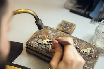 Image showing Close up hands of jeweller, goldsmiths making of golden ring with gemstone using professional tools.