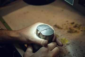 Image showing Close up hands of jeweller, goldsmiths making of golden ring with gemstone using professional tools.