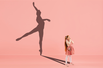 Image showing Childhood and dream about big and famous future. Conceptual image with girl and shadow of fit female ballet dancer on coral pink background