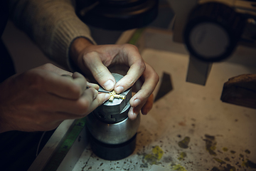 Image showing Close up hands of jeweller, goldsmiths making of golden cross with gemstone using professional tools.