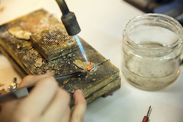 Image showing Close up hands of jeweller, goldsmiths making of golden ring with gemstone using professional tools.