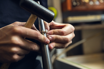 Image showing Close up hands of jeweller, goldsmiths making of golden ring with gemstone using professional tools.