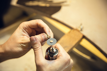 Image showing Close up hands of jeweller, goldsmiths making of silver ring with gemstone using professional tools.