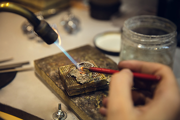 Image showing Close up hands of jeweller, goldsmiths making of silver ring with gemstone using professional tools.