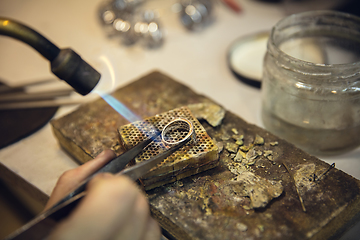 Image showing Close up hands of jeweller, goldsmiths making of silver ring with gemstone using professional tools.