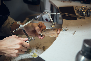 Image showing Close up hands of jeweller, goldsmiths making of silver ring with gemstone using professional tools.