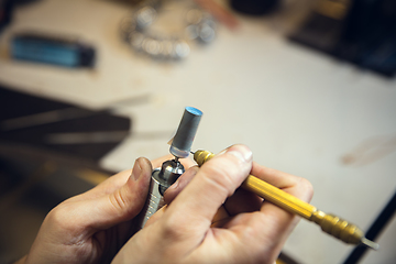 Image showing Close up hands of jeweller, goldsmiths making of silver ring with gemstone using professional tools.