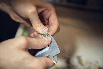 Image showing Close up hands of jeweller, goldsmiths making of silver ring with gemstone using professional tools.