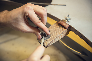 Image showing Close up hands of jeweller, goldsmiths making of silver ring with gemstone using professional tools.