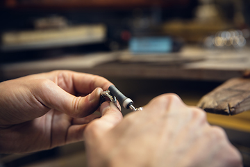 Image showing Close up hands of jeweller, goldsmiths making of silver ring with gemstone using professional tools.