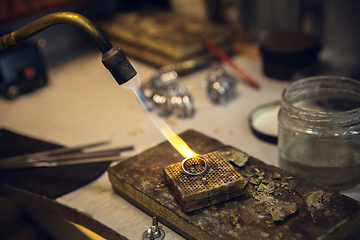 Image showing Close up hands of jeweller, goldsmiths making of silver ring with gemstone using professional tools.