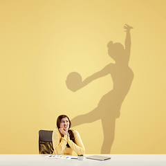 Image showing Young woman dreaming about future in big sport during her work in office. Becoming a legend. Shadow of dreams on the wall behind her. Copyspace.
