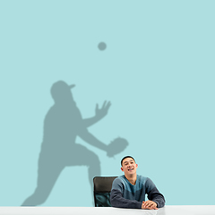 Image showing Young man dreaming about future in big sport during his work in office. Becoming a legend. Shadow of dreams on the wall behind him. Copyspace.