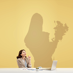 Image showing Young woman dreaming about future in floristics during her work in office. Becoming a legend. Shadow of dreams on the wall behind her. Copyspace.