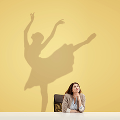 Image showing Young woman dreaming about future in big sport during her work in office. Becoming a legend. Shadow of dreams on the wall behind her. Copyspace.