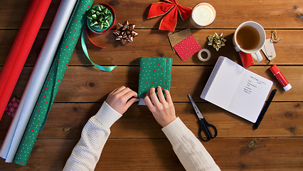 Image showing hands wrapping christmas gift into paper at home