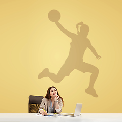 Image showing Young woman dreaming about future in big sport during her work in office. Becoming a legend. Shadow of dreams on the wall behind her. Copyspace.